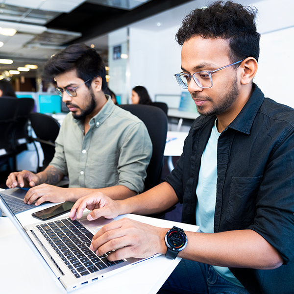 Two Capital One India associates sit at a desk and work on their laptops